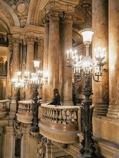 a woman sitting on top of a stone staircase next to chandeliers and lamps