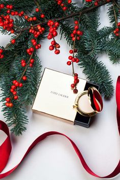 a christmas ornament with a ring on it next to red ribbon and evergreen branches