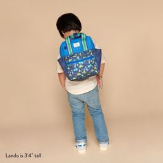 a young boy with a blue backpack on his back standing in front of a beige wall