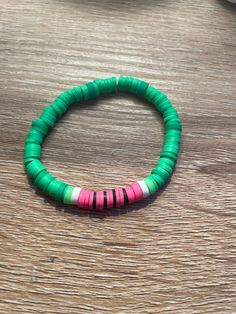 a green and pink beaded bracelet sitting on top of a wooden table