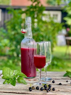 a bottle and glass filled with liquid sitting on top of a wooden table next to berries