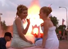 two young women sitting on top of a pink object with flames in the air behind them