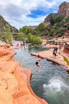 a person jumping into a river with people standing on the rocks and cliffs in the background