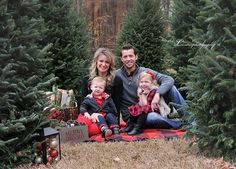 a family sitting on a blanket in front of christmas trees