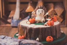 a hedgehog cake sitting on top of a tree stump with pumpkins around it