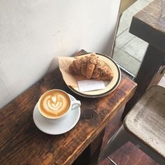 a cappuccino and pastry sit on a wooden table next to a chair