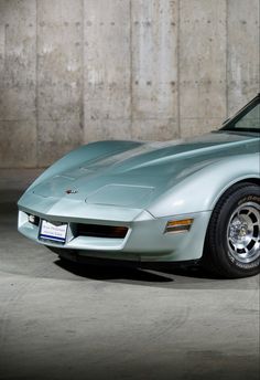 a silver sports car parked in a parking lot next to a concrete wall and cement floor