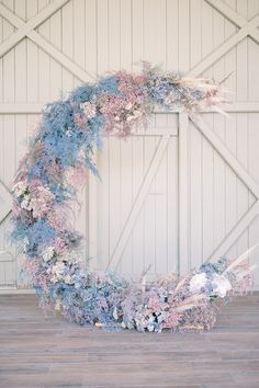 a wreath made out of blue and pink flowers on a wooden floor in front of a white wall