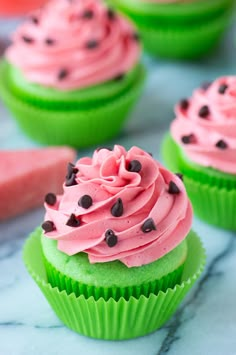 two green cupcakes with pink frosting and chocolate chips on top, sitting next to each other