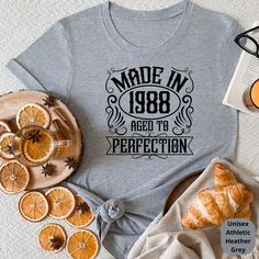 a gray shirt that says made in 1908 aged to perfectionion next to sliced oranges