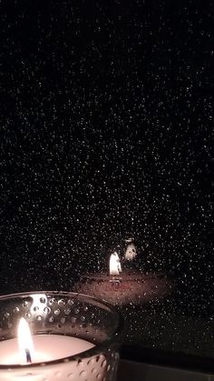 a lit candle sitting on top of a window sill next to a rain covered window