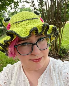 a woman with pink hair wearing a green crocheted hat and eyeglasses