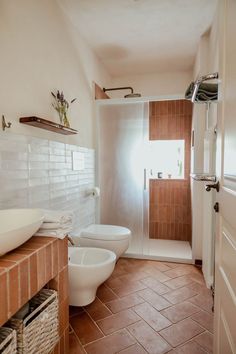 a white toilet sitting next to a sink in a bathroom under a window on top of a tiled floor