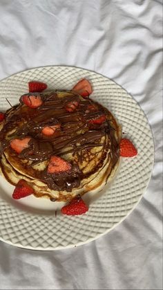 a white plate topped with pancakes covered in chocolate and strawberries