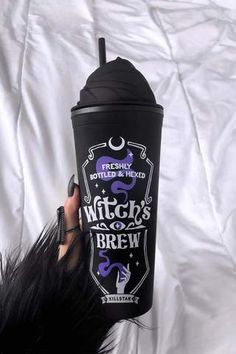 a woman holding up a black cup with purple writing on it and the words witch's brew