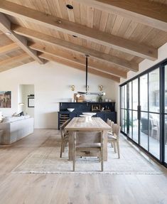 a woman walking through a living room with wooden floors and ceiling beams in the background