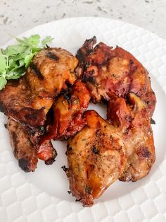 three pieces of meat on a white plate with parsley and cilantro garnish