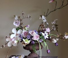 a vase filled with lots of flowers sitting on top of a wooden table next to a wall