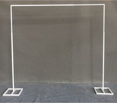 a white metal frame with two square bases on the floor in front of a gray wall