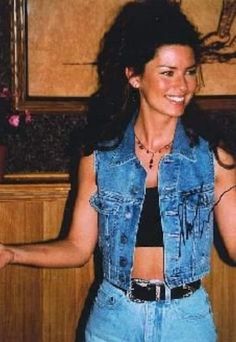 a woman with her arms out in front of the camera, wearing jeans and a denim vest