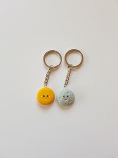 two keychains with faces on them sitting next to each other, one has a smiley face and the other has an orange