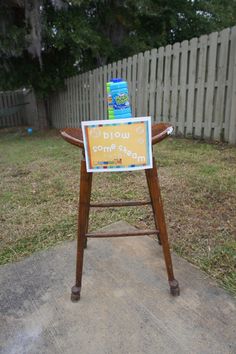 a sign sitting on top of a wooden chair in front of a fence and grass