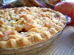 an apple pie sitting on top of a wooden table next to two apples and a person