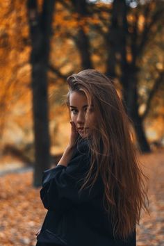 a woman with long hair is talking on her cell phone in an autumn park setting