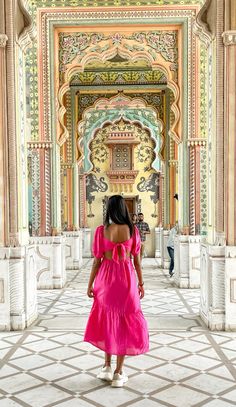 a woman in a pink dress is walking through an ornate building