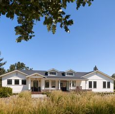 a large white house sitting on top of a lush green field next to tall grass