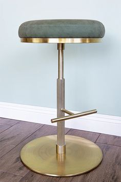 a gold metal stool with a green cushion on the back and foot rests on a wooden floor