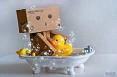 a cardboard box sitting on top of a bathtub filled with bubbles and rubber ducks