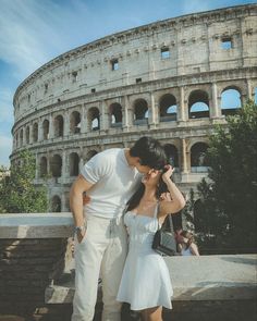 a man and woman standing next to each other in front of an old building with the roman colossion behind them