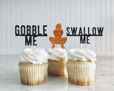 three cupcakes with white frosting and gold sparklers on top are sitting in front of a sign that says gobble swallow me