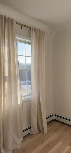 an empty room with wood floors and white curtains