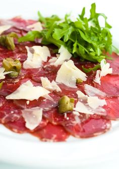 a white plate topped with meat and veggies next to parmesan cheese