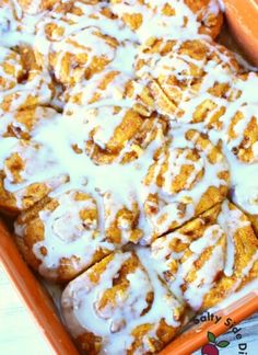 an orange pan filled with cinnamon rolls covered in icing and sitting on a table