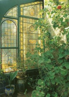 an old stained glass window surrounded by greenery and potted plants in front of it