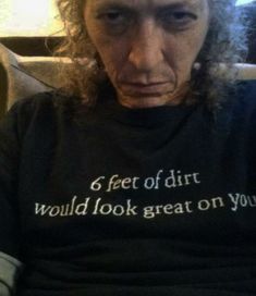 a man with long curly hair wearing a shirt that says 6 feet of dirt would look great on you