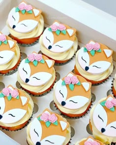 cupcakes with frosting decorated as foxes and flowers in a box on a table