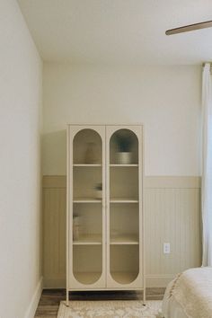 a white cabinet sitting in the corner of a room next to a bed and window