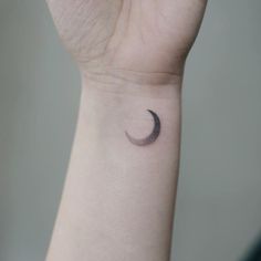 a small crescent tattoo on the wrist is shown in black and grey colors, with a tiny dot at the center