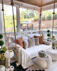 a porch with white furniture and lots of pillows on it's swing bed, surrounded by potted plants