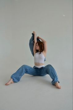 a woman in white shirt and jeans sitting on the floor with her arms up above her head