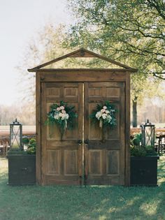 two wooden doors with wreaths and flowers on them in front of an outdoor venue