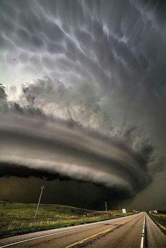 an image of a storm coming in from the sky over a road and grassy field