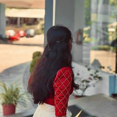 a woman with long black hair wearing a red and white dress standing in front of a building