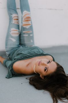 a woman laying on the ground with her legs crossed and wearing ripped leggings