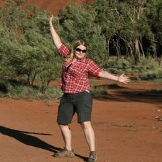 a woman in plaid shirt throwing a frisbee on dirt field next to trees