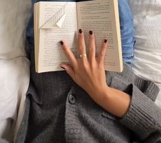 a woman is reading a book while laying on the bed with her hand resting on an open book